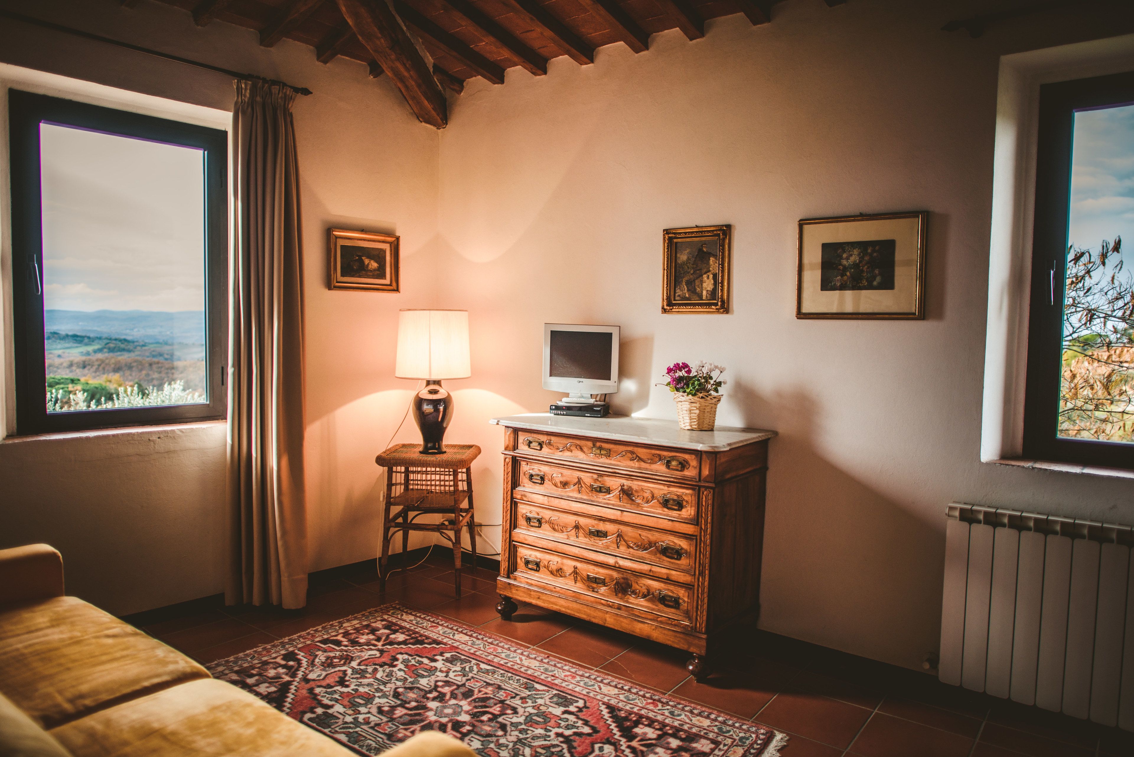 A cozy room with a large window, a wooden dresser, a lamp, and a television.