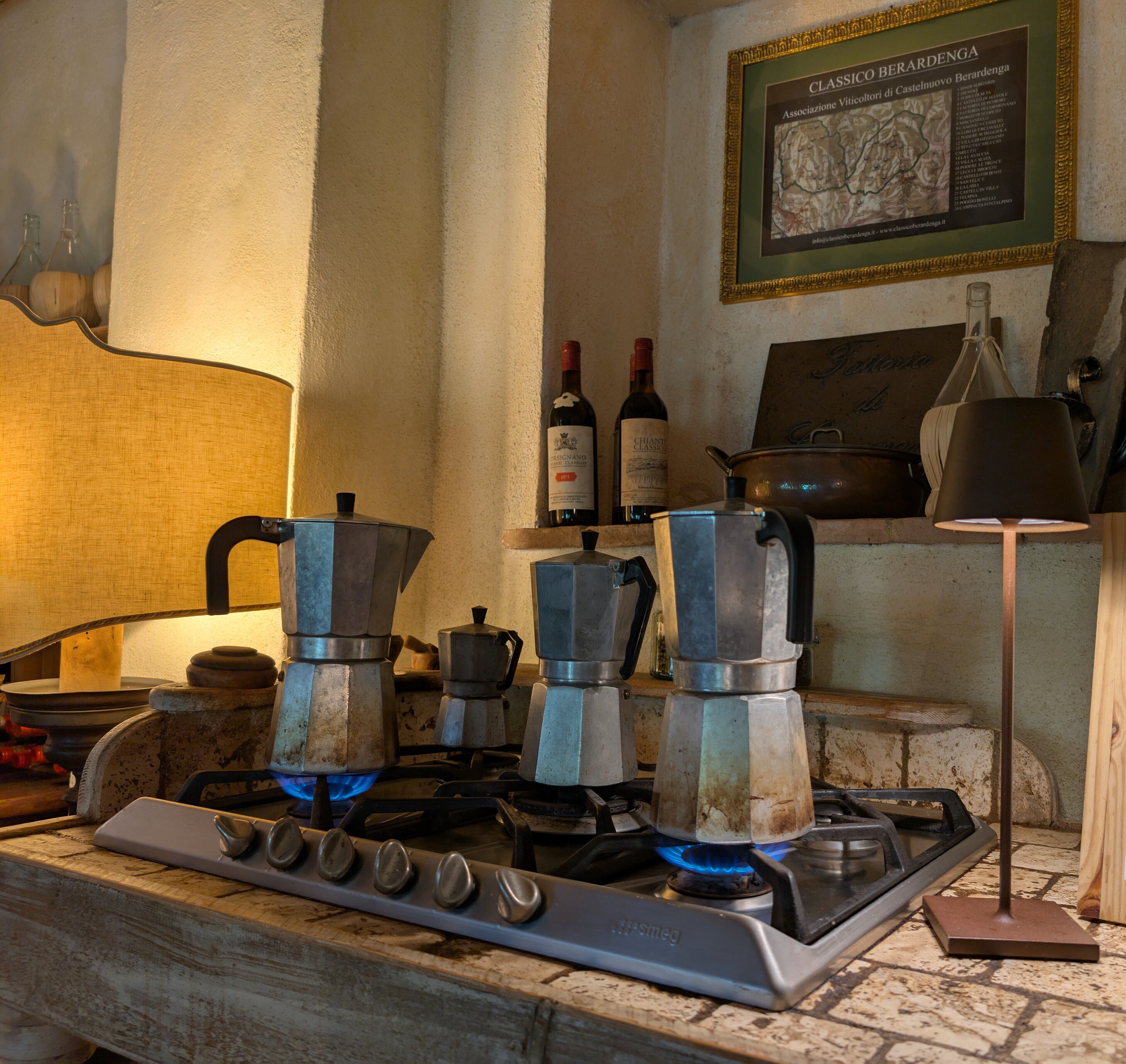 Una cocina con estufa a gas, cafeteras, botellas de vino y un mapa enmarcado en la pared.