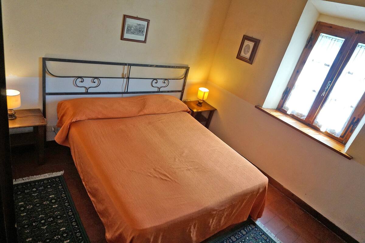 Un lit bien fait, avec une couvre-lit orange, une lampe de chevet et un tableau encadré au mur.