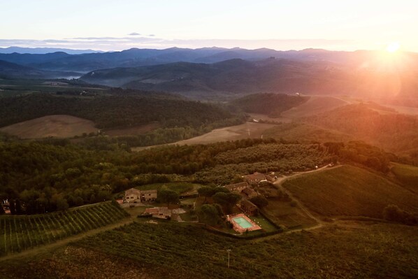 Vista aérea de uma paisagem rural com colinas onduladas, um pequeno conjunto de edifícios e uma piscina.