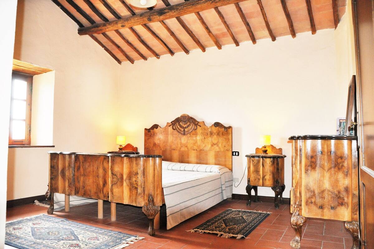 Une chambre à coucher avec un lit en bois, deux tables de chevet, une commode et une grande fenêtre.