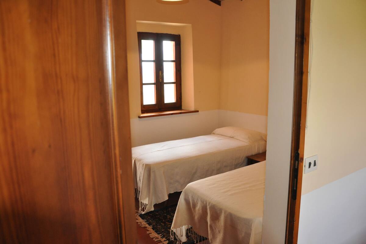 Une petite chambre d’hôtel composée d’une seule pièce, avec deux lits simples, une fenêtre et une porte.