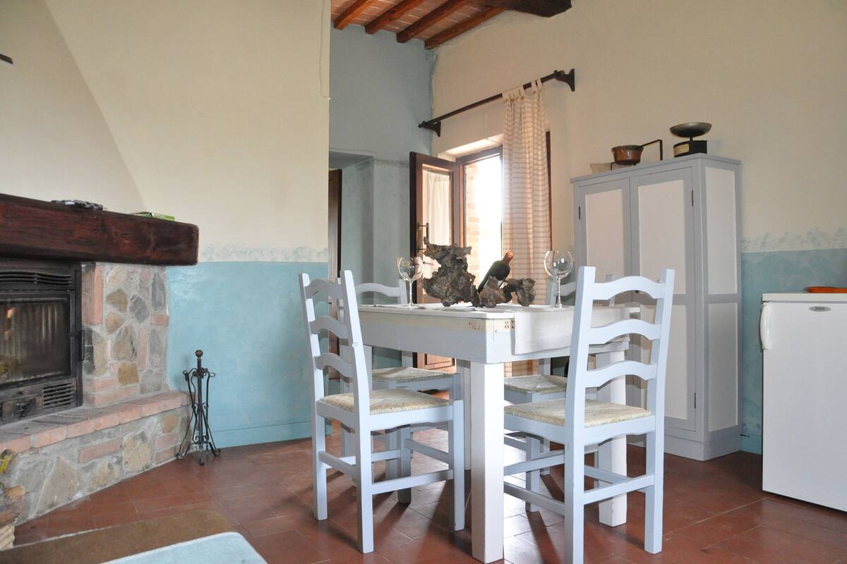 Un coin repas agrémenté d’une cheminée en pierre, d’une table en bois blanc et de chaises.
