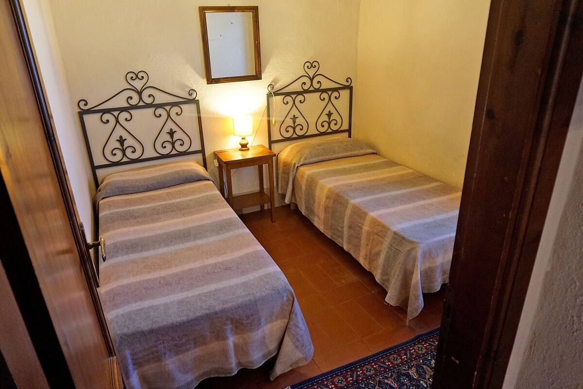 Une petite chambre confortable avec deux lits simples, une table de chevet avec une lampe et un miroir au mur.