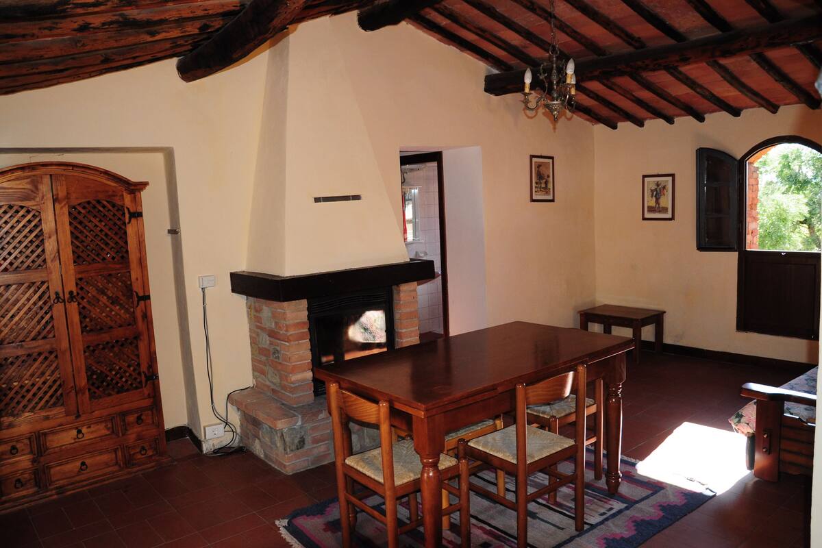 Un coin repas agrémenté d’une cheminée en briques, d’une table et de chaises en bois, et offrant une vue sur l’extérieur grâce à une fenêtre ouverte.