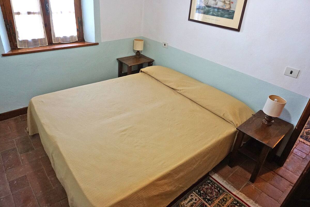 Une chambre à coucher comprenant un lit, une table de chevet, une lampe, une fenêtre et un tableau accroché au mur.