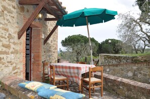 A rustic outdoor seating area with a table and chairs, a green umbrella, and a stone wall.