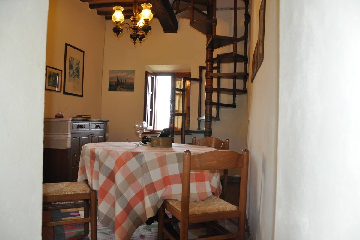 Un coin repas avec une nappe à carreaux, des chaises en bois, un lustre et un escalier.