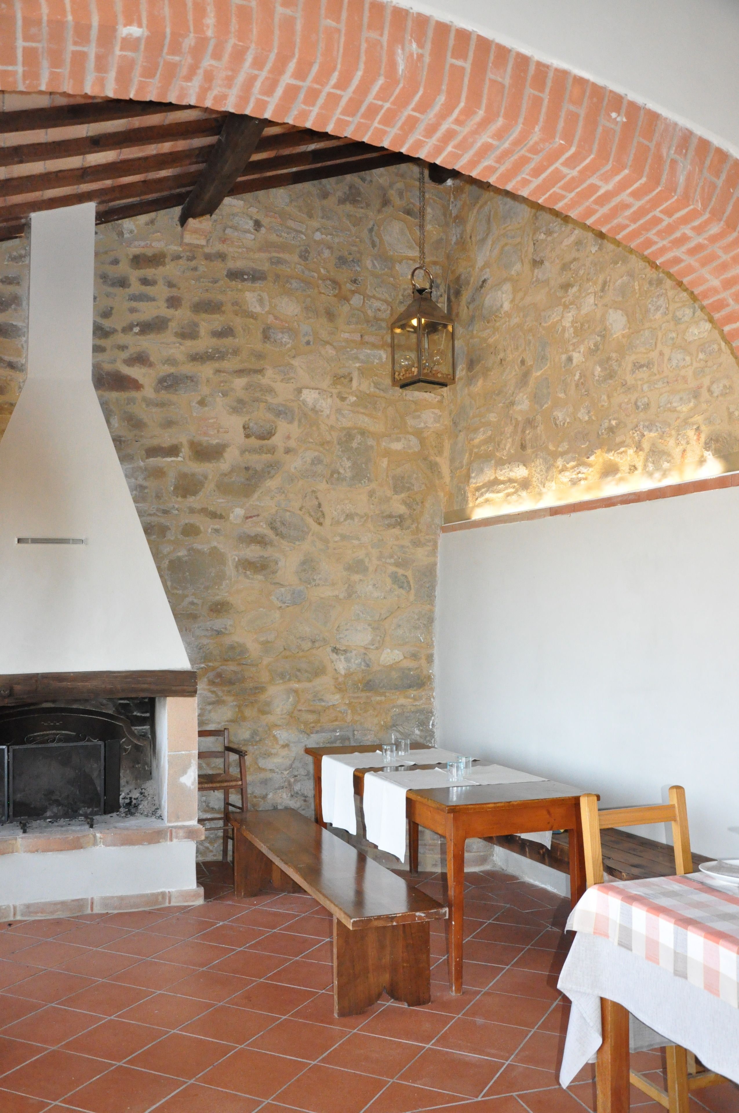 A stone-walled room with a fireplace, wooden benches, and a table set for dining.
