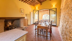A rustic dining area with a brick fireplace, wooden beams, and a stone wall. - Tenuta di Monaciano (Castelnuovo Berardenga)