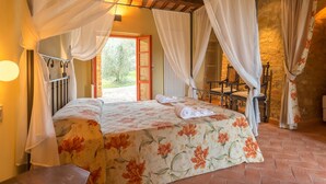A bedroom with a bed, curtains, a chair, and a view of the outdoors. - Tenuta di Monaciano (Castelnuovo Berardenga)