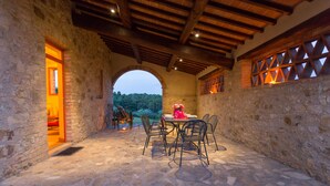 An outdoor patio with stone flooring, a table with chairs, and a view of greenery through an archway. - Tenuta di Monaciano (Castelnuovo Berardenga)