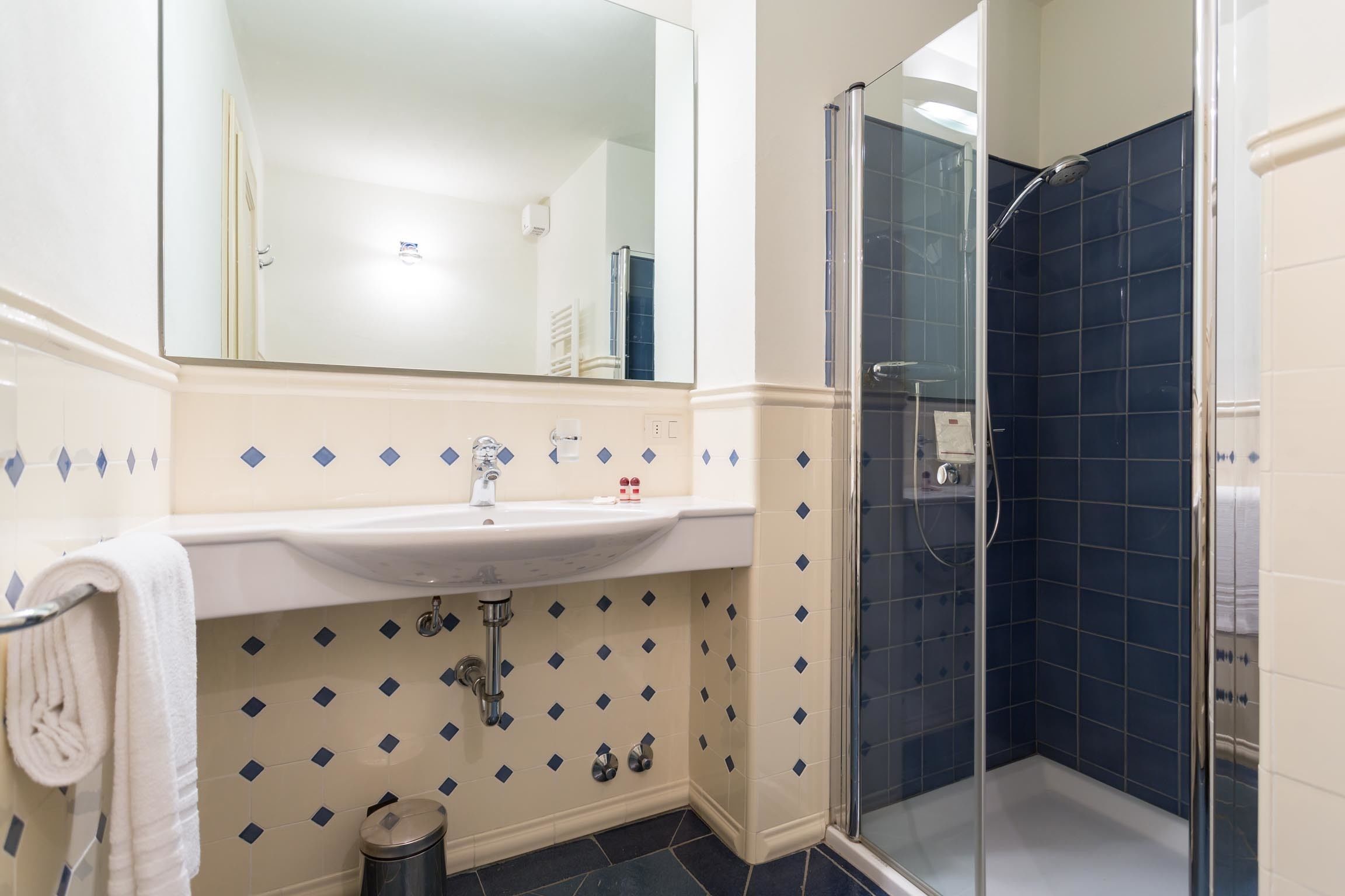 A bathroom with a white sink, a mirror, a glass shower enclosure, and blue diamond-patterned tiles.