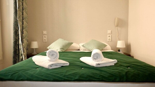 Una cama bien hecha con ropa de cama verde, dos toallas enrolladas y dos almohadas, una verde y otra blanca.