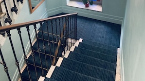 Una escalera con barandillas negras y pasamanos, que conduce a un rellano con un ventanal de vidrieras.