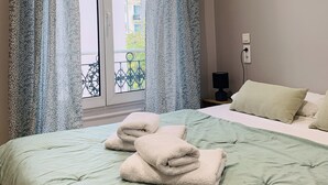 Una habitación de hotel con cama, dos almohadas, mesita de noche con lámpara y ventana con cortinas.
