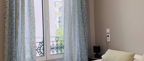 A hotel room with a bed, two pillows, a bedside table with a lamp, and a window with curtains.