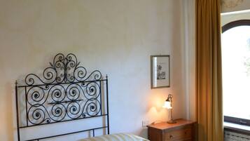 A bedroom with a metal headboard, a bedside table with a lamp, and a window with curtains.