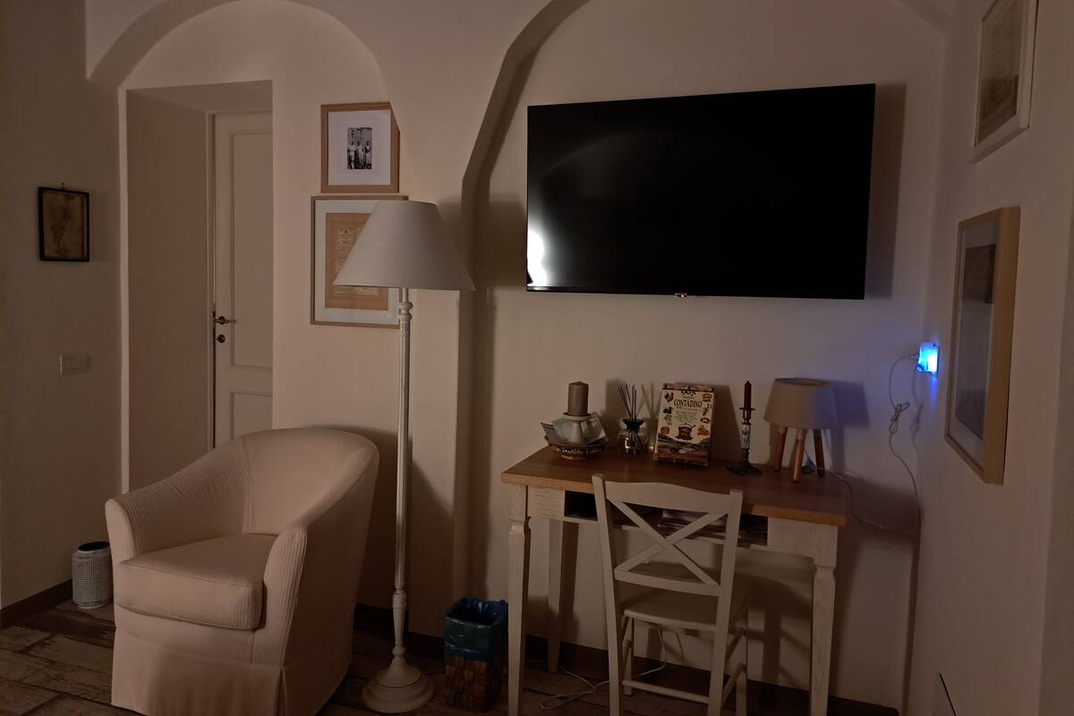 Een woonkamer met een aan de muur bevestigde televisie, een bank, een tafel met decoratieve objecten en een lamp.