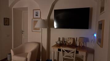 A living room with a TV mounted on the wall, a sofa, a table with decorative items, and a lamp.