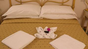 Una cama con una colcha amarilla estampada, dos toallas blancas y un arreglo floral sobre la cama.