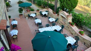 An outdoor patio with multiple tables and chairs, surrounded by stone walls and potted plants.