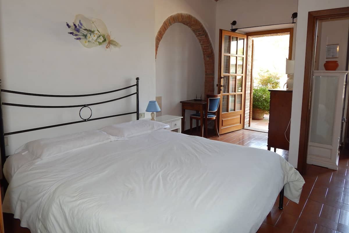 Un dormitorio con cama, escritorio y silla. Hay una puerta que da a un área exterior.