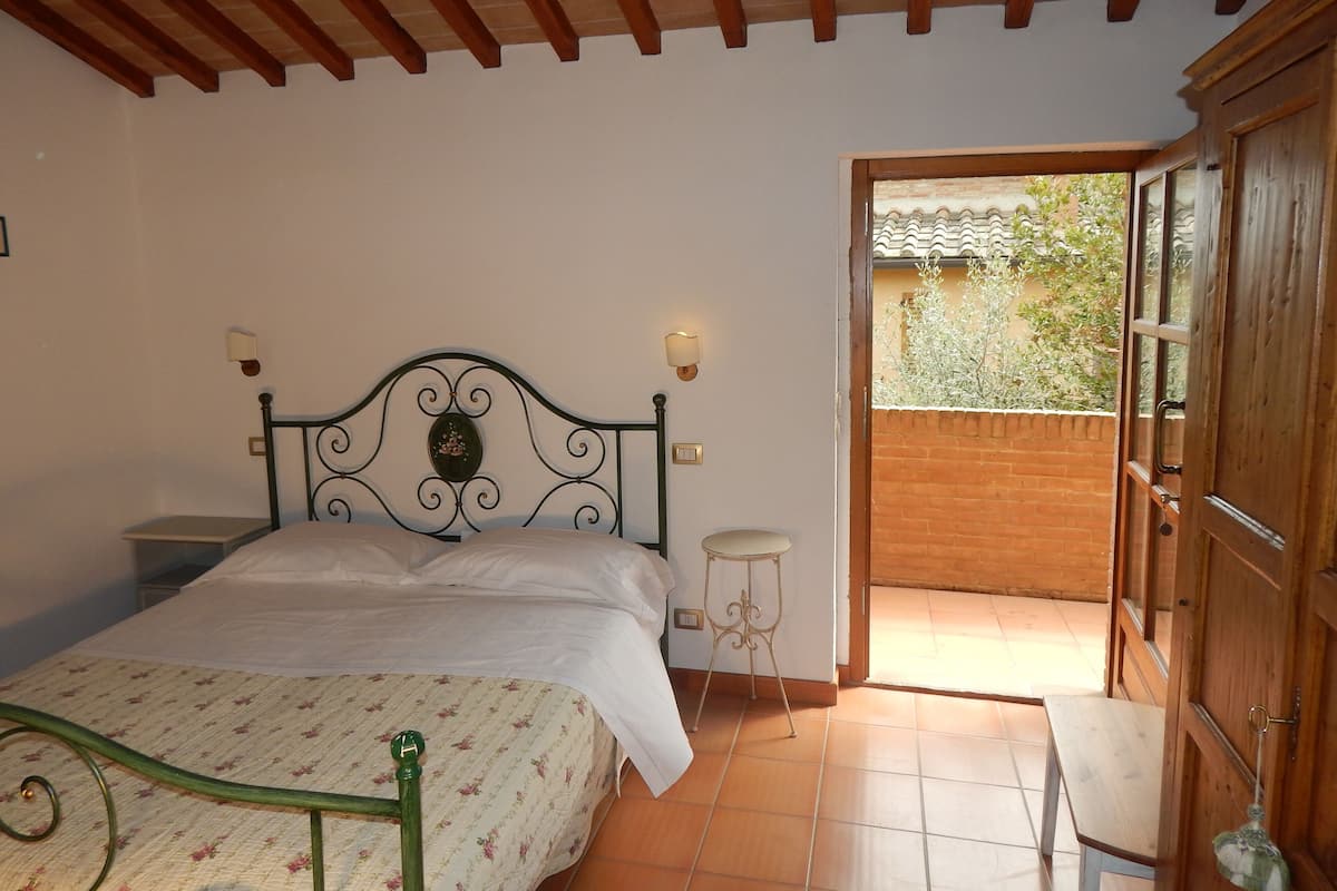 Un dormitorio con cama, mesita de noche, lámpara de pared y puerta de madera que da a un espacio exterior.