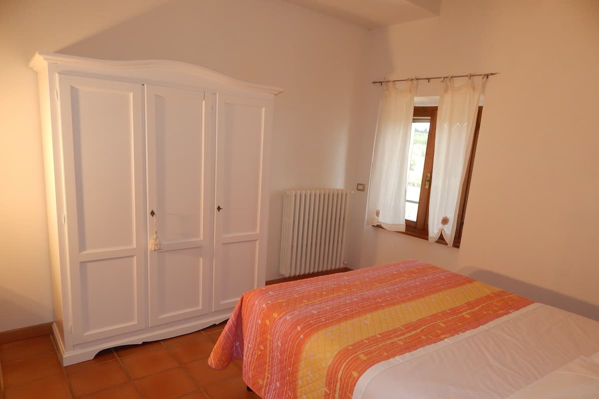 Un dormitorio con cama, armario, radiador y ventana con cortinas.
