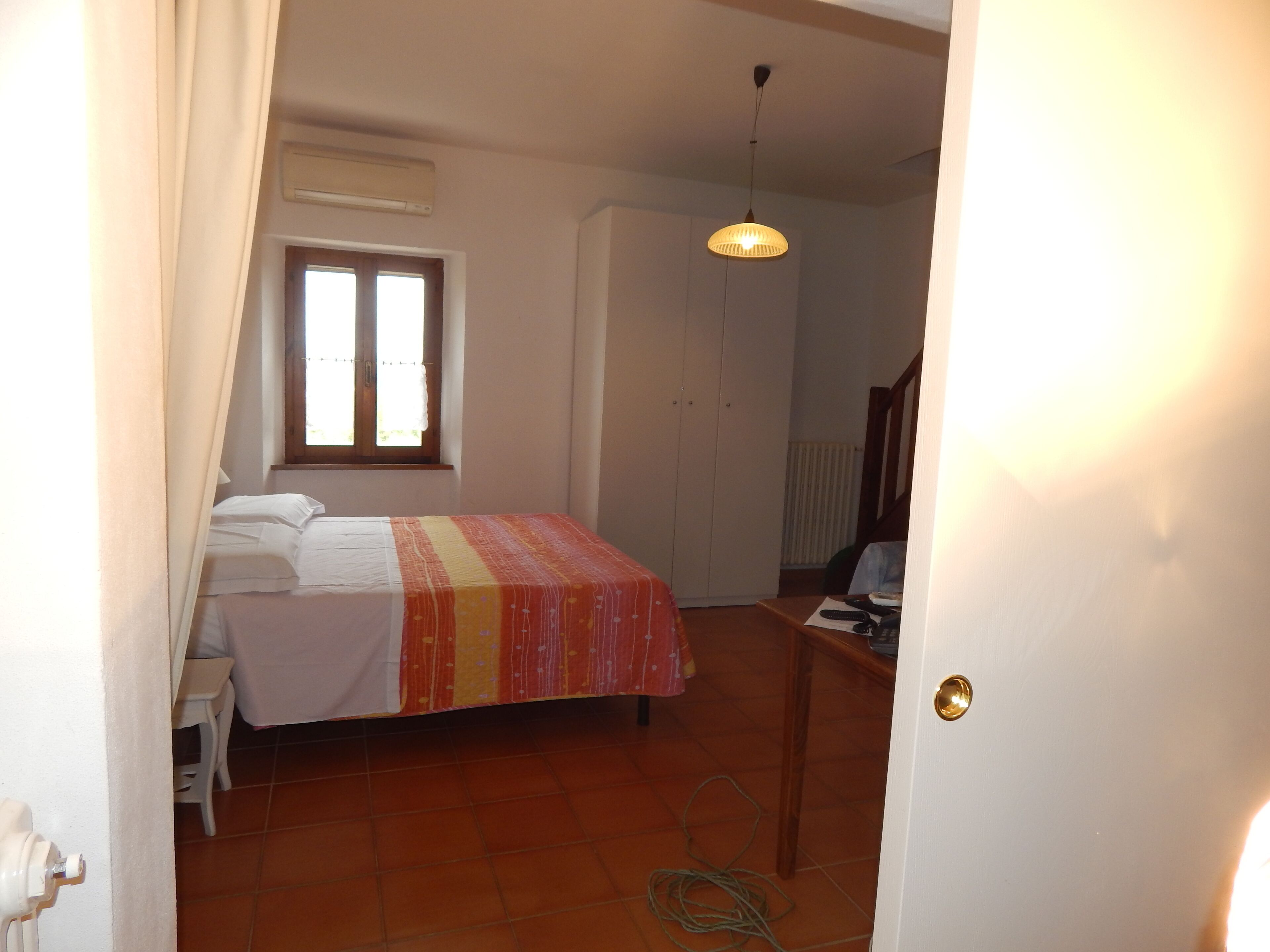 A bedroom with a bed, a window, a wardrobe, and a desk with a lamp.