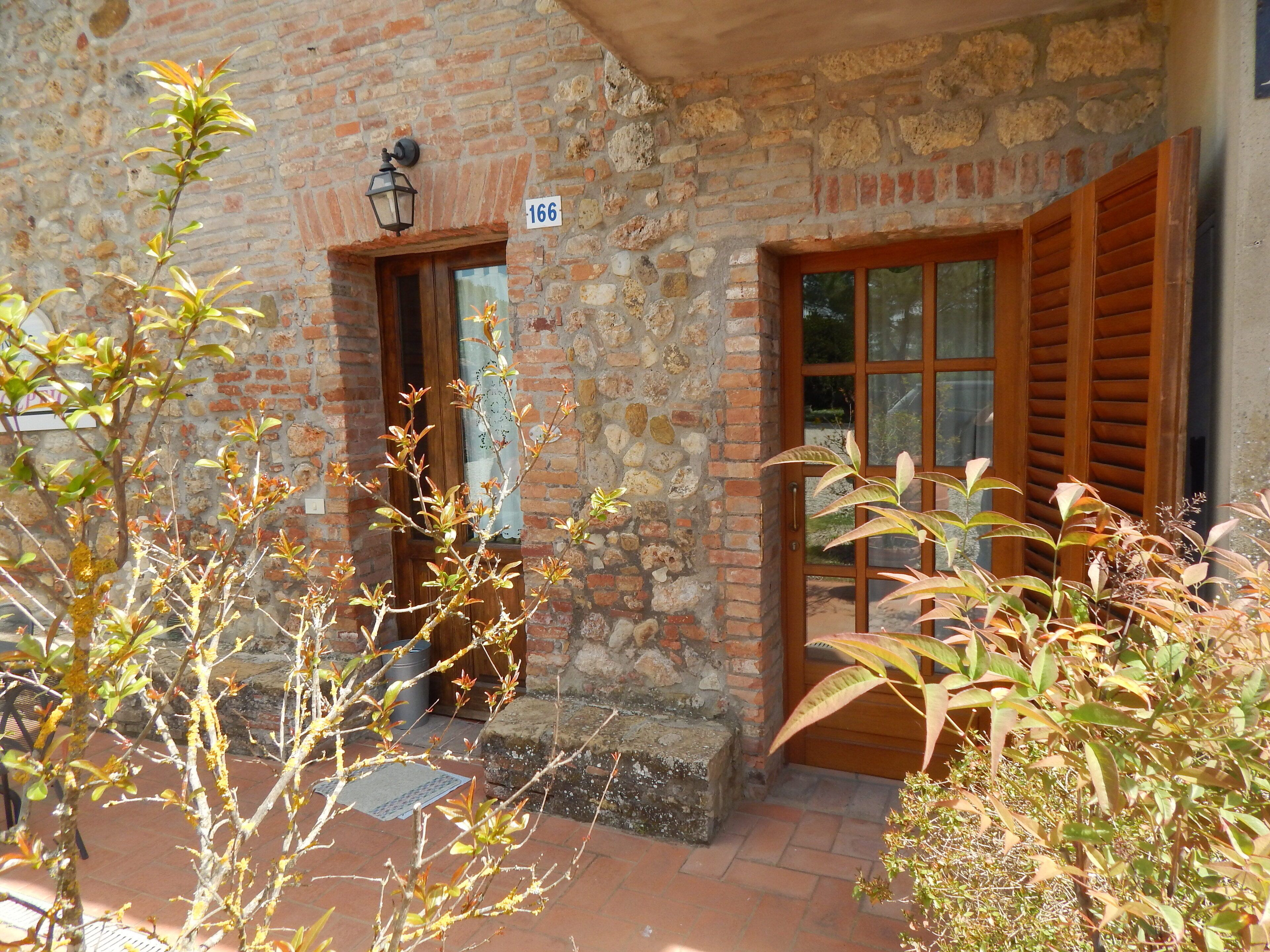 A stone building with a wooden door and window shutters, a number plaque, and a small step leading to the entrance.