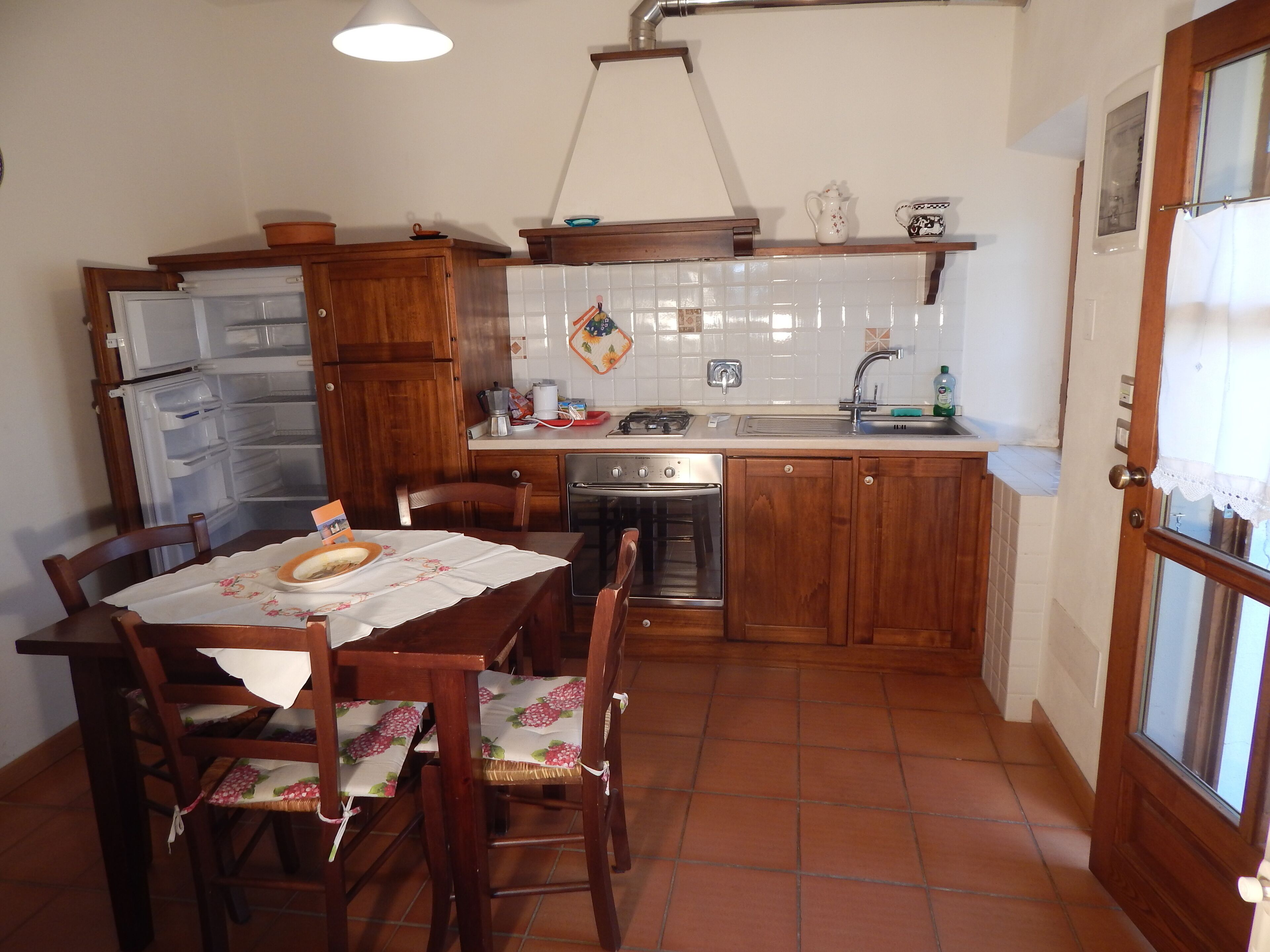 A compact kitchen with wooden cabinets, a built-in oven, a sink, and a dining table set with chairs.