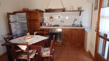 A compact kitchen with wooden cabinets, a built-in oven, a sink, and a dining table set with chairs.