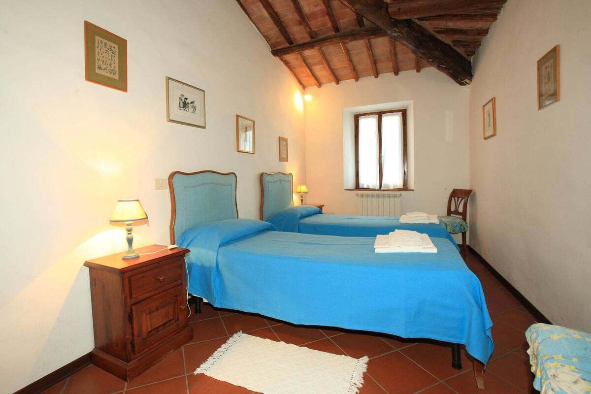 A bedroom with two beds, a wooden cabinet, a window with curtains, and a white rug on the floor.