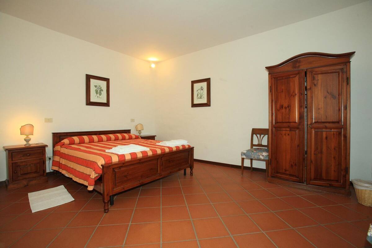 A bedroom with a wooden bed, two bedside tables with lamps, a wooden wardrobe, and two framed pictures on the walls.