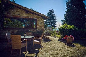 A stone building with a patio area featuring wicker chairs and a table with wine glasses.