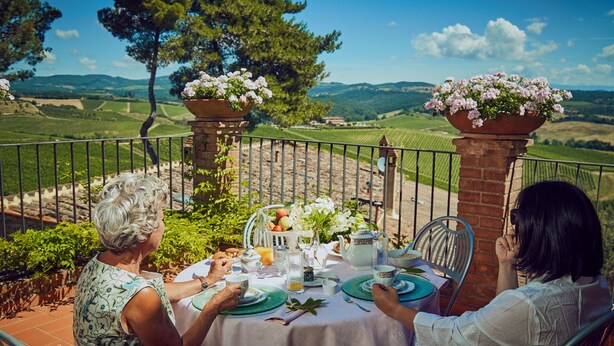 A dining table set outdoors with a scenic view of rolling hills and vineyards. - Il Poderaccio (Siena)