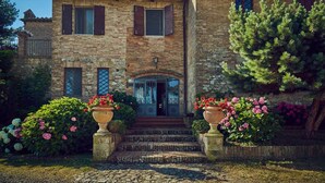 A stone building with a tiled roof, a central entrance with steps, and potted plants with pink flowers. - Il Poderaccio (Siena)