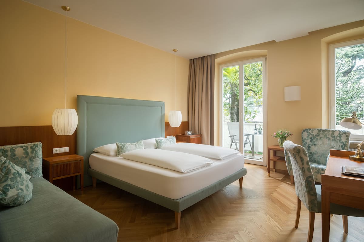 Quarto de hotel com uma cama grande, uma escrivaninha, uma cadeira e vista para o exterior.