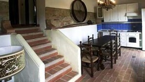 A rustic kitchen with a stone wall, wooden staircase, and a dining table with chairs. - La Grotta di Montecchino (Siena)