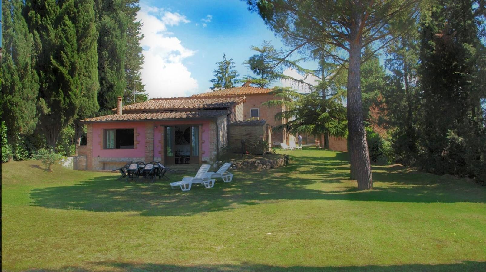 Una casa con techo de tejas, un patio con sillas y un jardín.