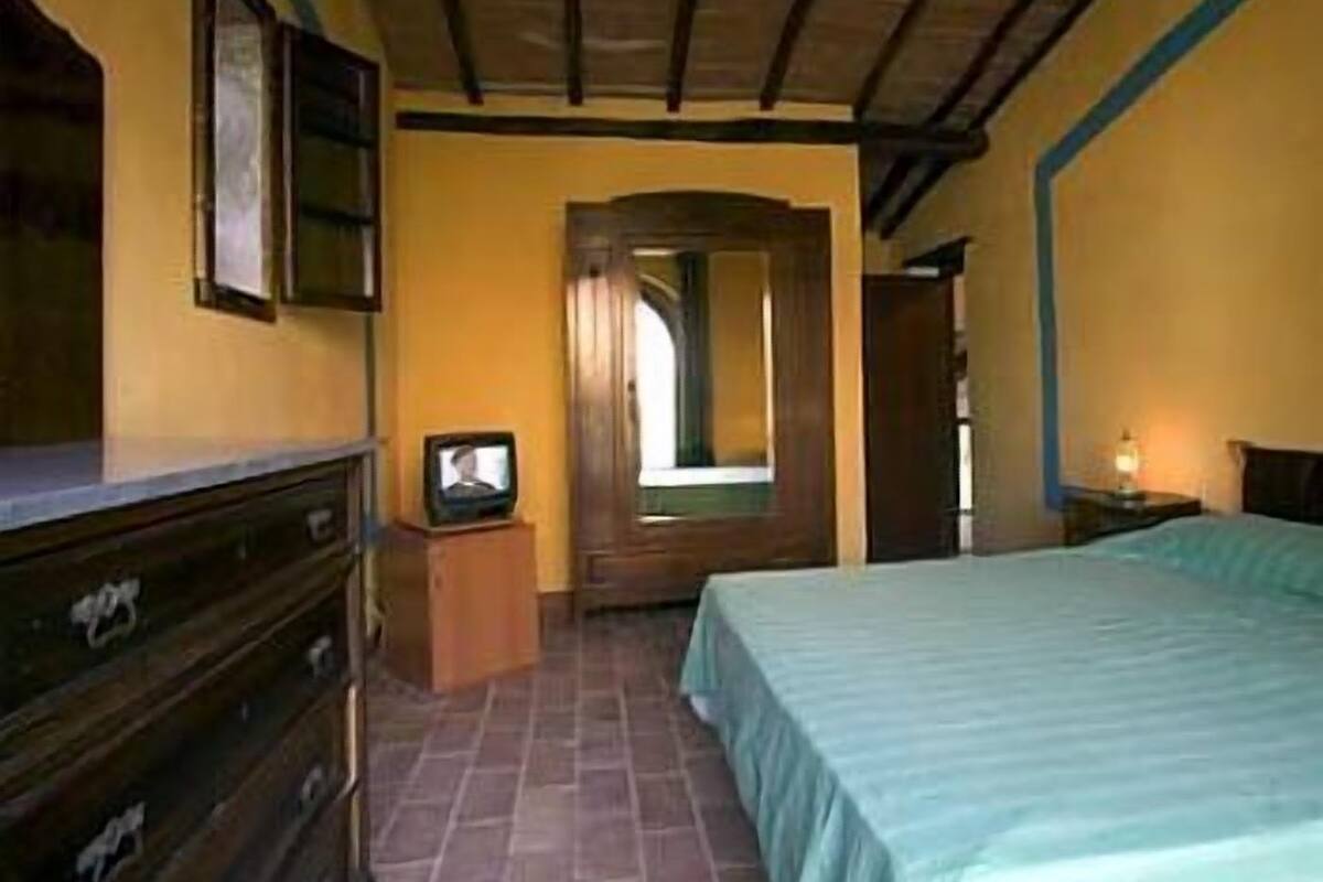 A bedroom with a bed, wooden dresser, and a television on a small table.