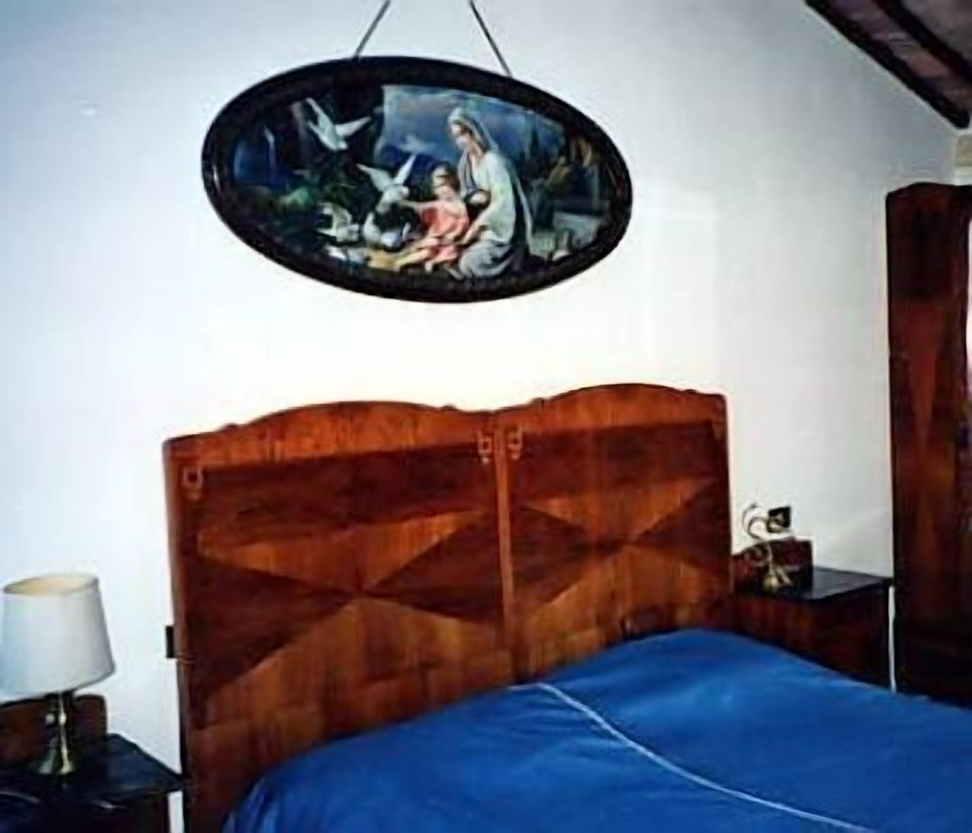 A bedroom with a wooden headboard, a blue bedspread, and a wall-mounted painting.