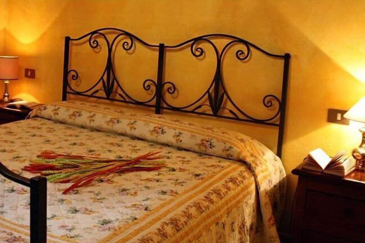 A bed with a floral bedspread and a decorative headboard, a nightstand with a lamp, and a wall-mounted light fixture.