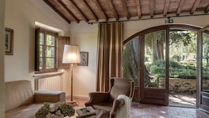 A cozy room with a wooden ceiling, a sofa, a chair, a lamp, and a view of a garden through a glass door. - Borgo al Cerro (Casole d'Elsa)
