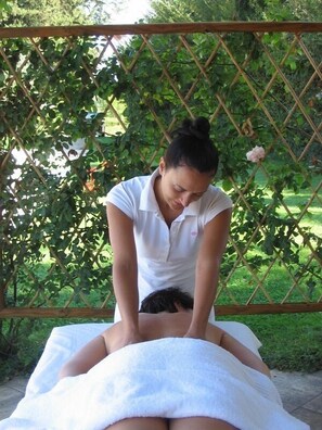A person receiving a back massage outdoors, with a wooden lattice fence and greenery in the background. - Borgo al Cerro (Casole d'Elsa)