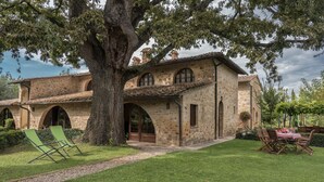 A stone house with a large tree in the front yard, a patio with chairs, and a table. - Borgo al Cerro (Casole d'Elsa)