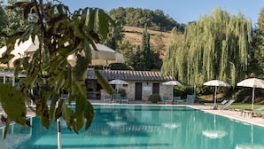 A clear swimming pool with lounge chairs and umbrellas, surrounded by stone buildings and trees. - Borgo al Cerro (Casole d'Elsa)