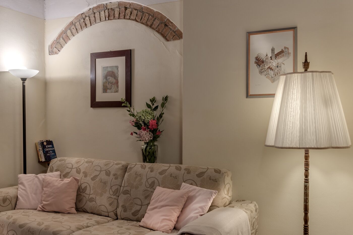 Una sala de estar acogedora con un sofá, una lámpara, un cuadro enmarcado y un jarrón con flores.