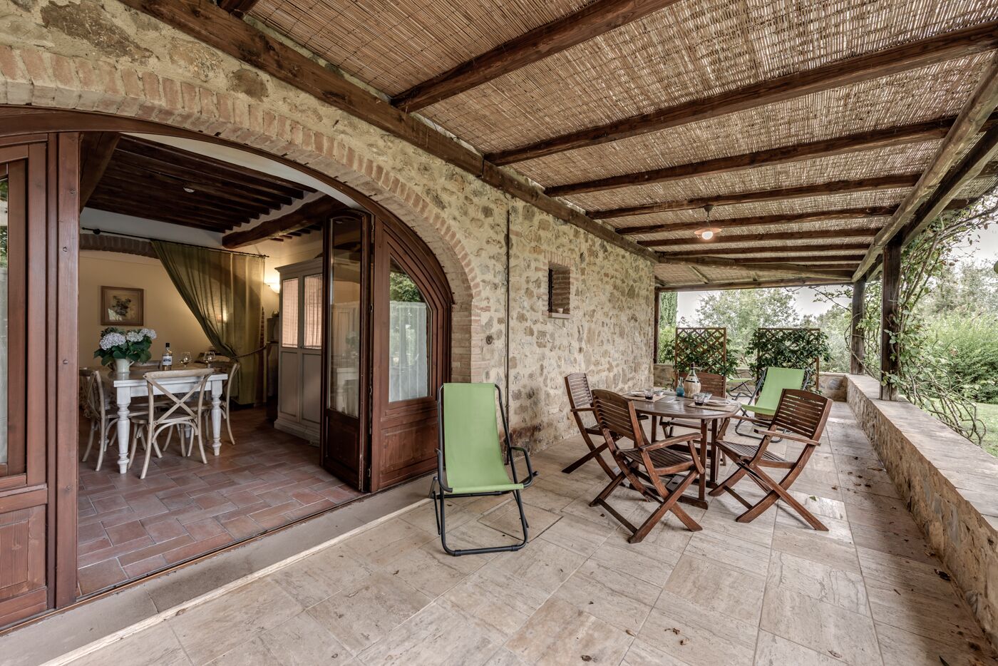 A covered patio with stone walls and wooden beams, featuring a table and chairs set for dining.